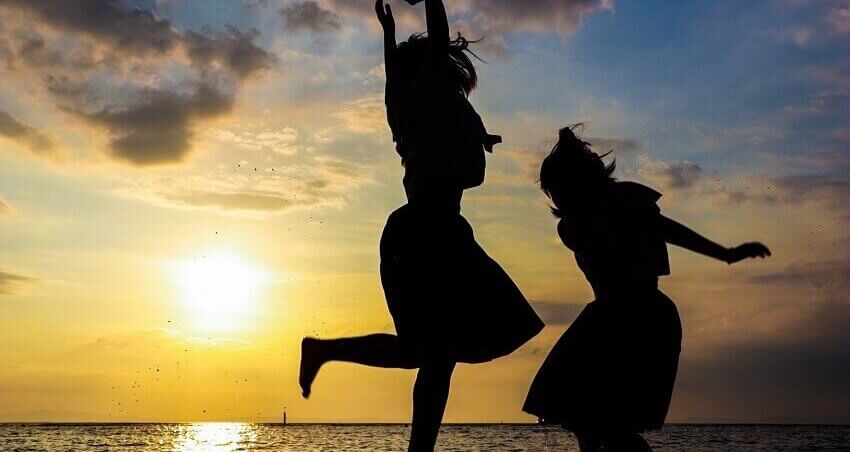 海岸で夕日をバックにはしゃぐ女性二人